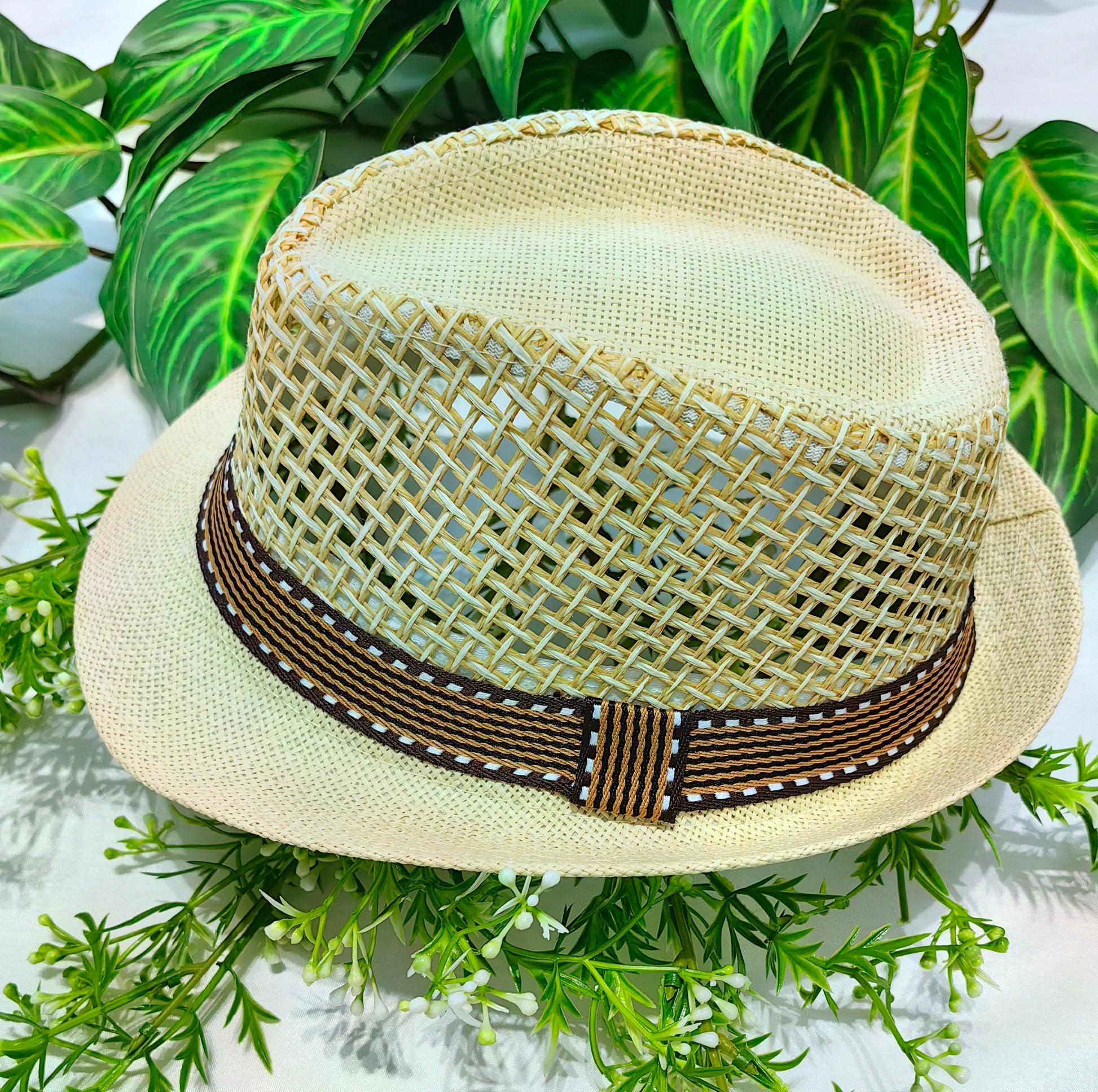 Beige straw hat with a brown woven band on a green leaf background