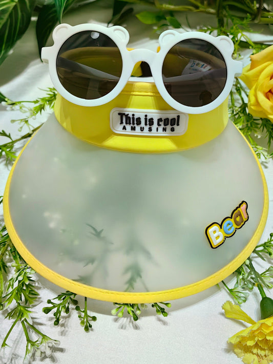 Yellow and gray children's hat with sunglasses on a green leafy background