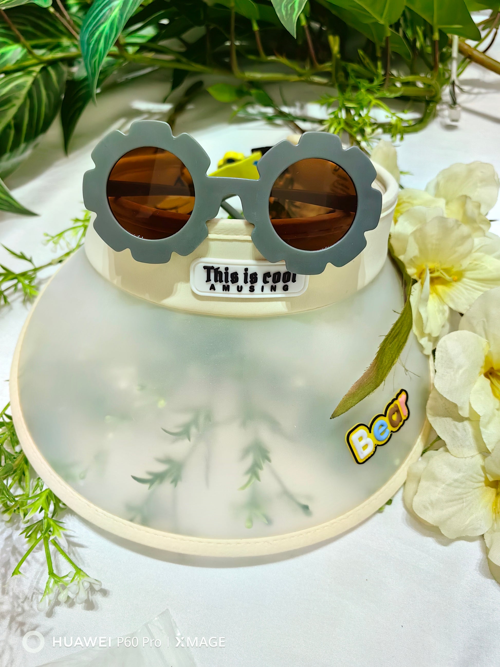 Summer cap with sunglasses on a white surface with greenery and flowers